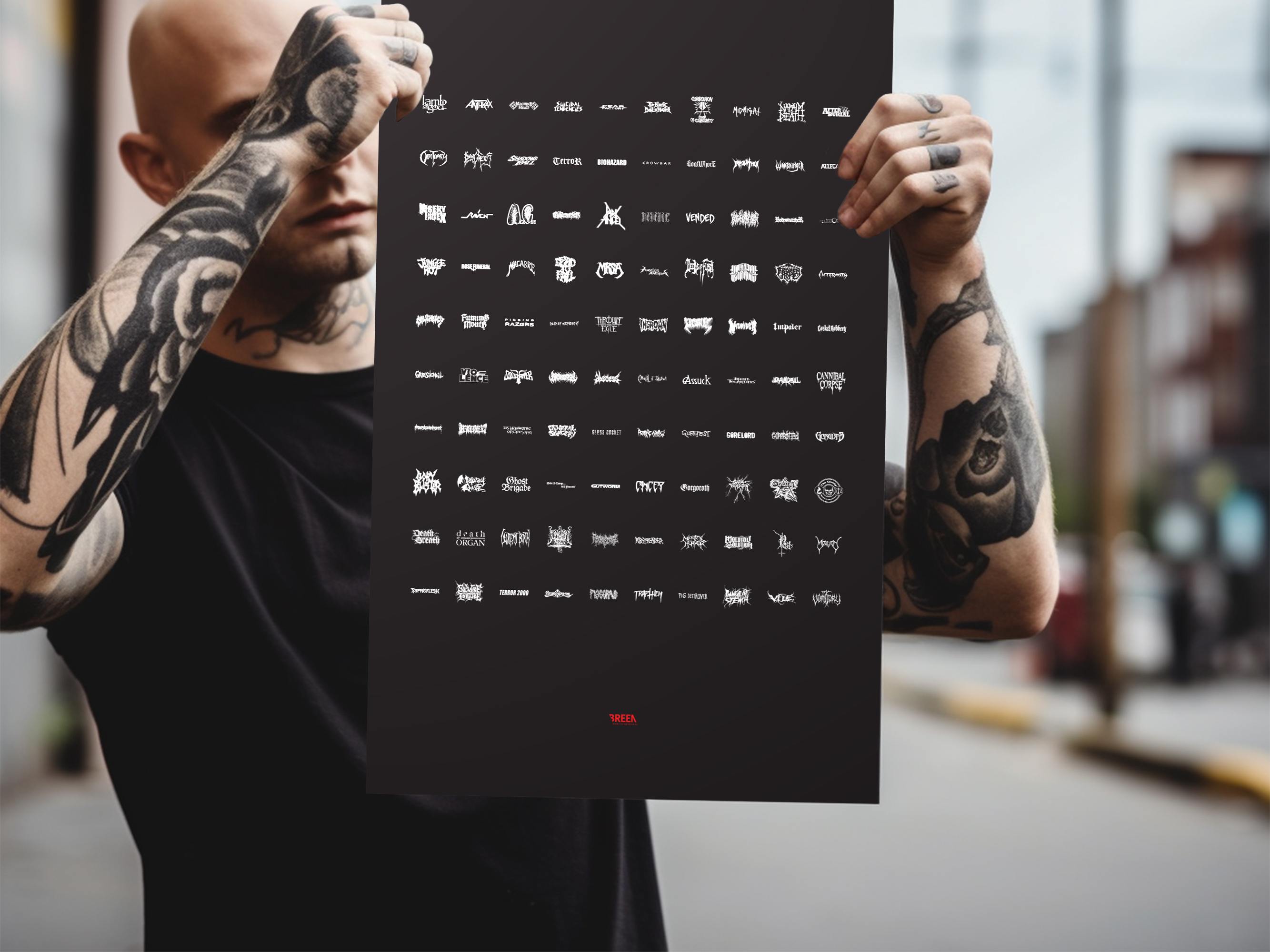 Man holding a black poster outside on the street. The man's arms are covered in tattoo's and he's wearing a black t-shirt. The poster he's holding features 100 metal band logo names organised in rows of 10.